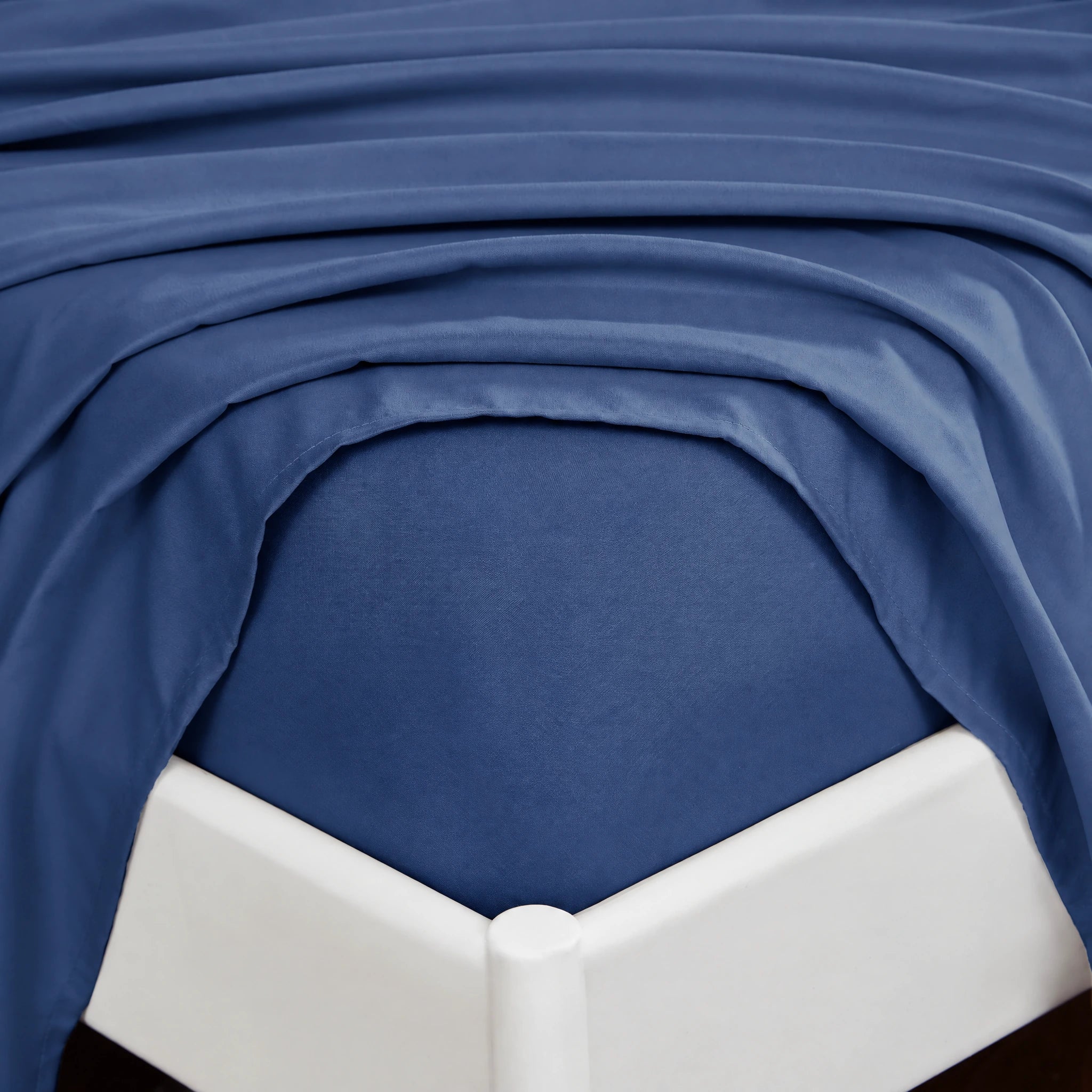 Navy fitted sheet wrapping around the corner of a mattress